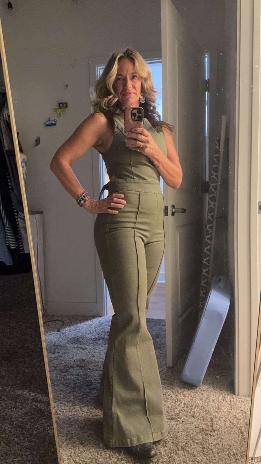 Samantha in an olive flared jumpsuit, taking a mirror photo